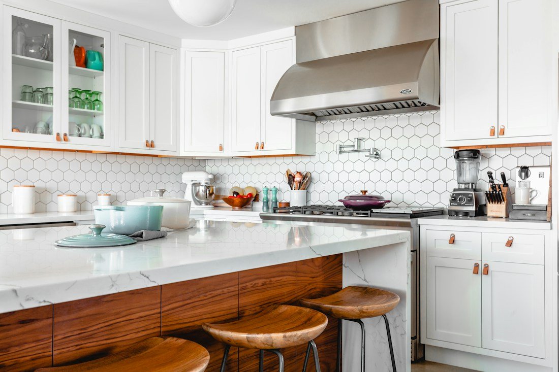 Cocina blanca con isla de madera, bancos y revestimiento geométrico